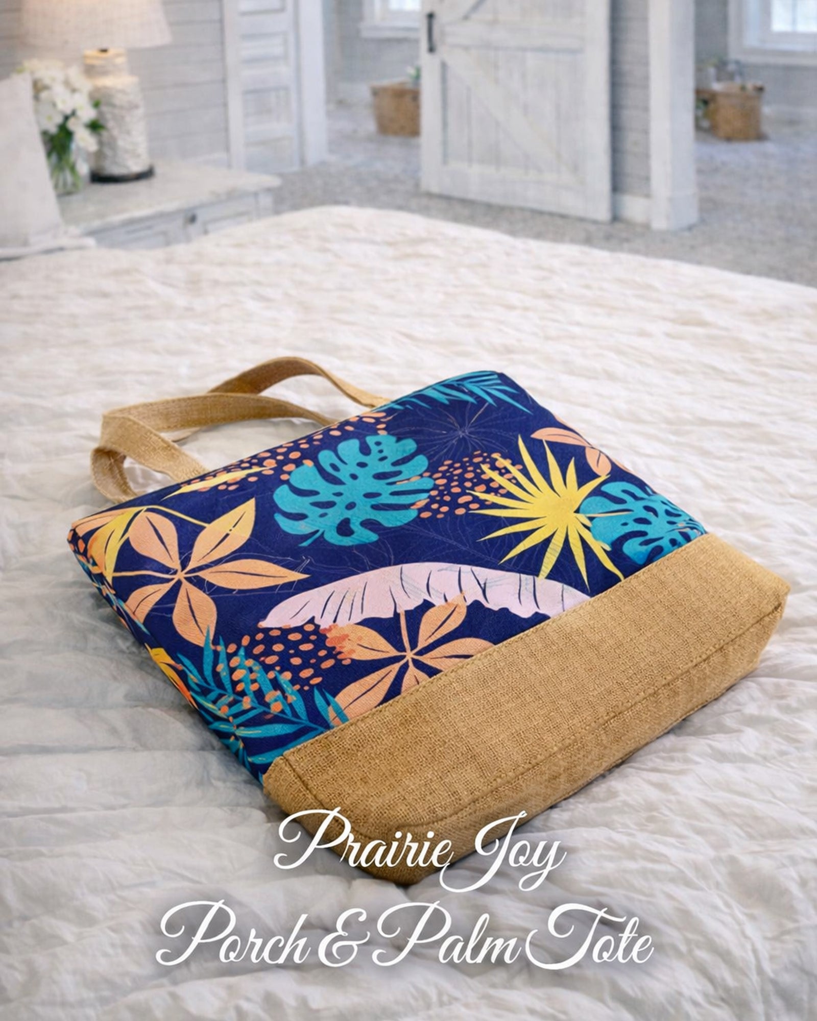 Prairiejoy Porch & Palm Tote Bag lying flat on a bed showing colorful leaf print and natural base